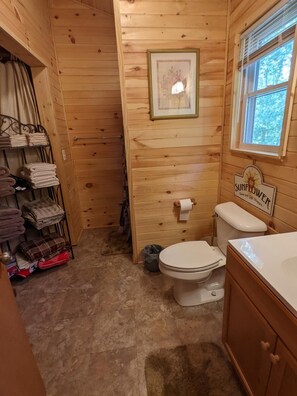 Une salle de bain aux murs lambrissés, équipée de toilettes, d’un lavabo et d’un porte-serviettes où sont pliées des serviettes.