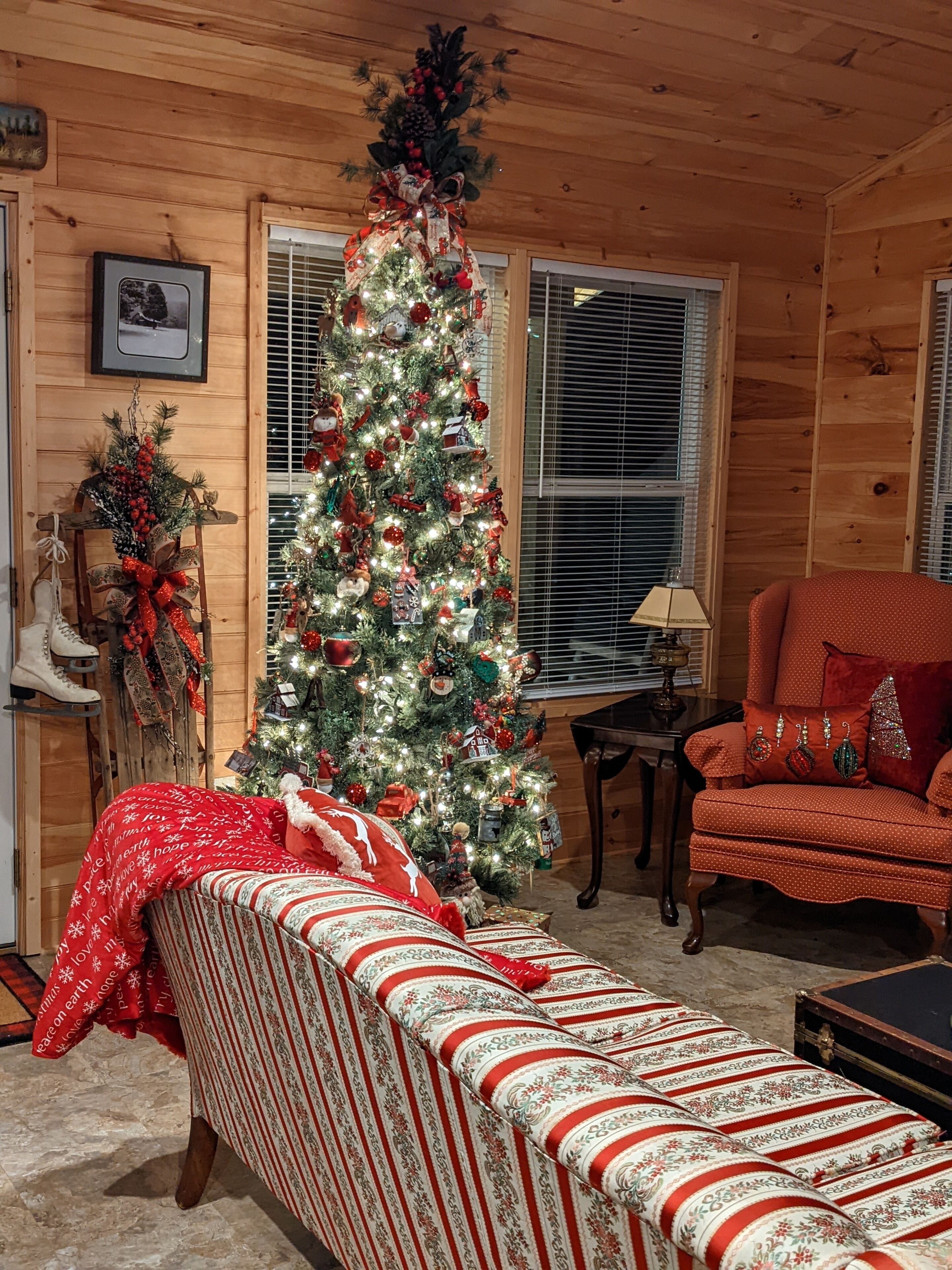 Un interior de cabaña acogedor con un árbol de Navidad decorado, un sofá a rayas y un sillón rojo.