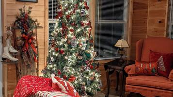 Un interior de cabaña acogedor con un árbol de Navidad decorado, un sofá a rayas y un sillón rojo.