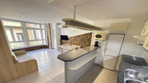 A modern kitchen with a granite countertop, stainless steel sink, and built-in appliances. There is a dining area with a table and chairs, and a seating area with a bench. - Agi Pi Sunyer 4 2D Apartamento for rent in Roses Girona. (Roses)
