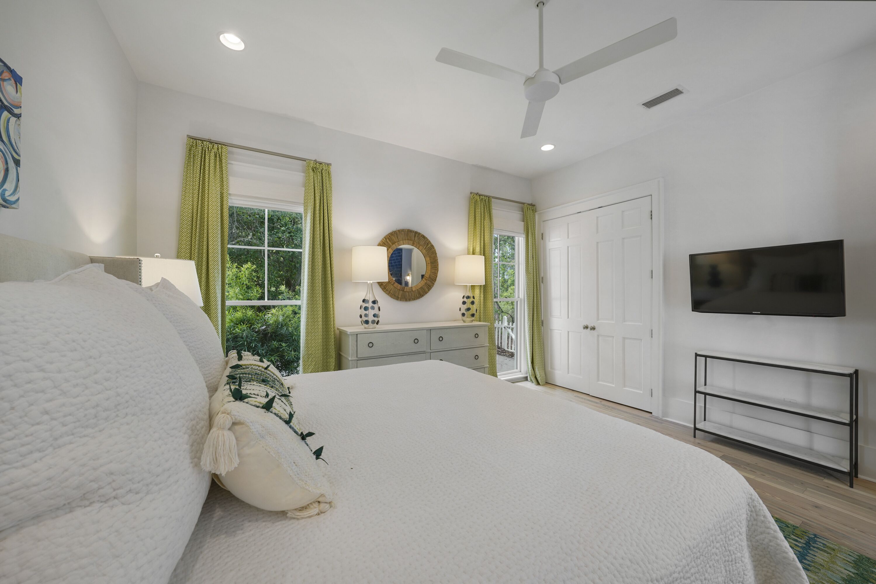 A bedroom with a large bed, a dresser, a mirror, a television, and a ceiling fan.