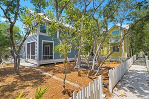 A residential area with two houses, one blue and one yellow, surrounded by trees and a white picket fence. - 6 Houses to Beach in Seaside, Screened Porch, Steps to Restaurants + 2 Bikes! (Santa Rosa Beach)