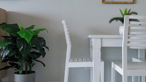 A white chair, a white table, and a potted plant in a room with a light-colored wall and a framed picture. - Ocean View 49A Wi-Fi Pool King bed (Airlie Beach)