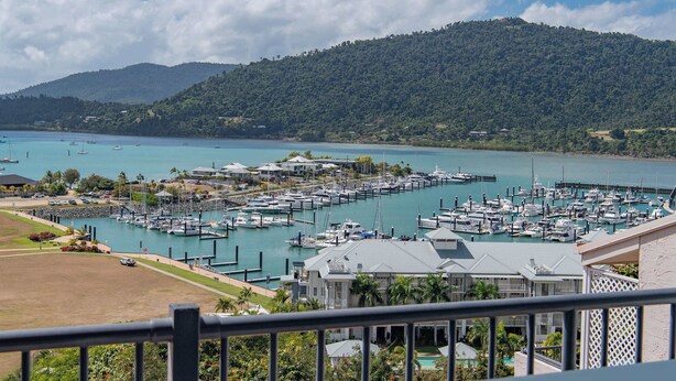 A marina with boats docked, surrounded by lush greenery and hills. - Ocean View 49A Wi-Fi Pool King bed (Airlie Beach)