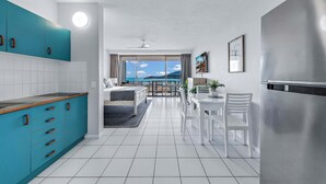 A modern kitchen with a teal cabinet, white tiled floor, and a view of the sea through large windows. - Ocean View 49A Wi-Fi Pool King bed (Airlie Beach)