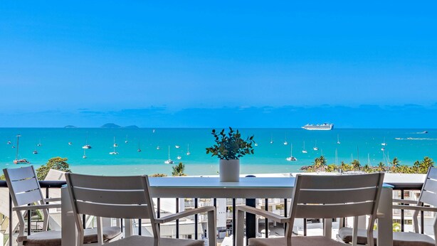 Eine Terrasse mit Blick auf das Meer, ausgestattet mit einem Tisch, Stühlen und einem Blumentopf.