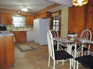 A kitchen with wooden cabinets, a white refrigerator, a dining table with chairs, and a ceiling fan.