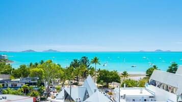 A coastal town with a prominent white building with a triangular roof, a visible sign for 'The Roundabout Shopping Centre', and a clear view of the turquoise sea with boats.