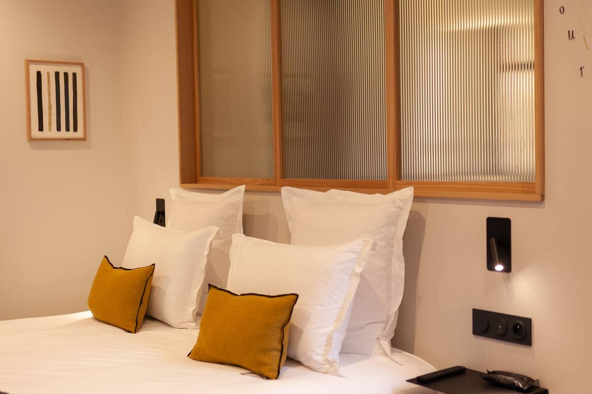 A modern bedroom with a large bed, a bedside table, a wall-mounted light, and a window with blinds.