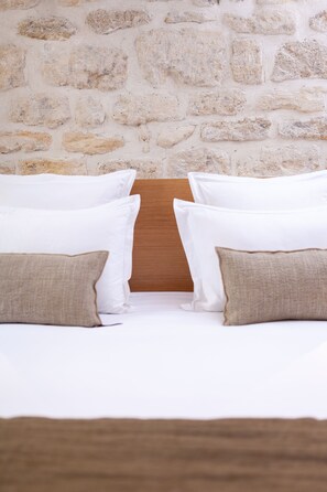 A bed with white and beige pillows, a wooden headboard, and a stone wall background. - Tinah - Champs Elysées (Paris)