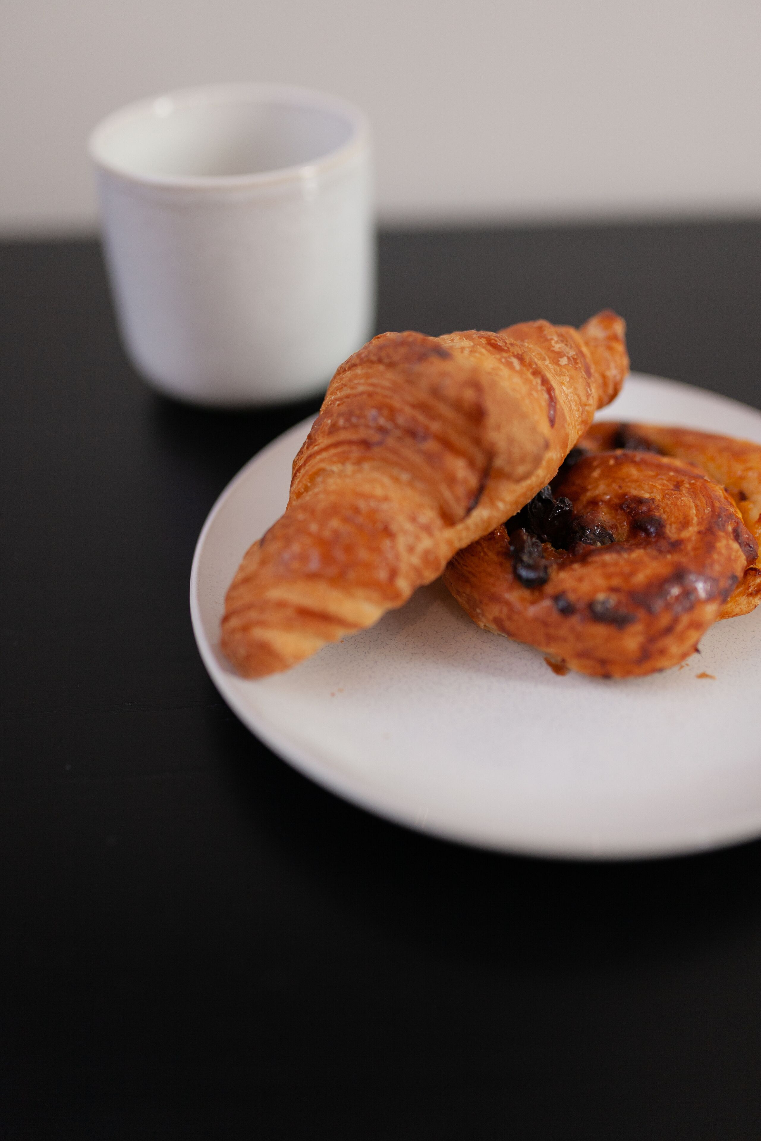 A plate with two pastries and a white cup on a black surface.