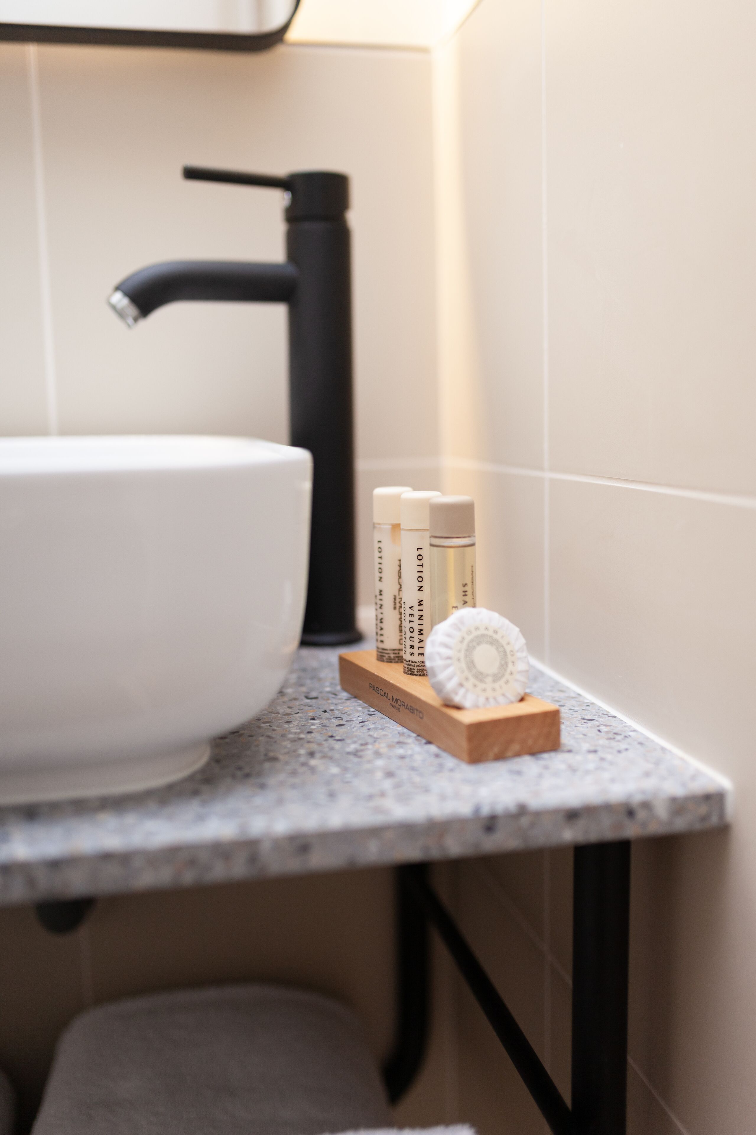 Une salle de bain avec un lavabo blanc, un robinet noir et des articles de toilette disposés sur un plateau en bois.