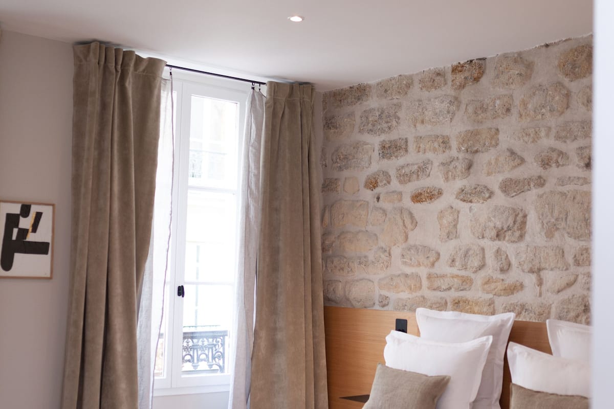A bedroom with a stone wall, a large bed with white bedding, and a wooden headboard.