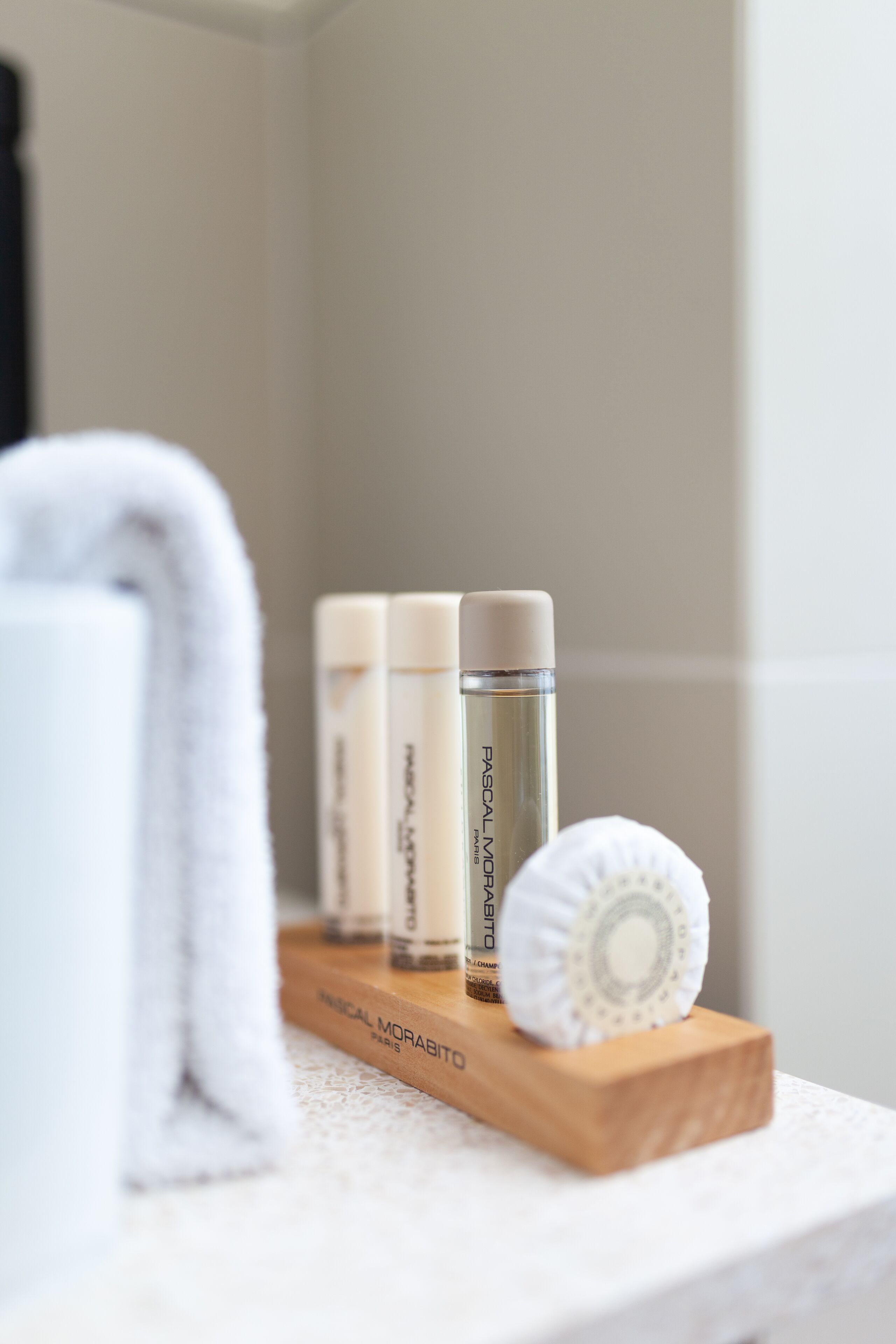 Une salle de bain avec une étagère en bois sur laquelle sont posés une serviette blanche, une éponge de bain blanche et deux flacons de crème hydratante pour le visage.