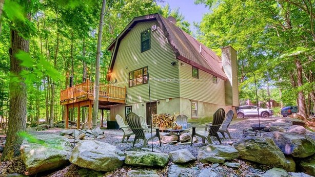 A rustic cabin with a porch, outdoor seating, and a forest backdrop.