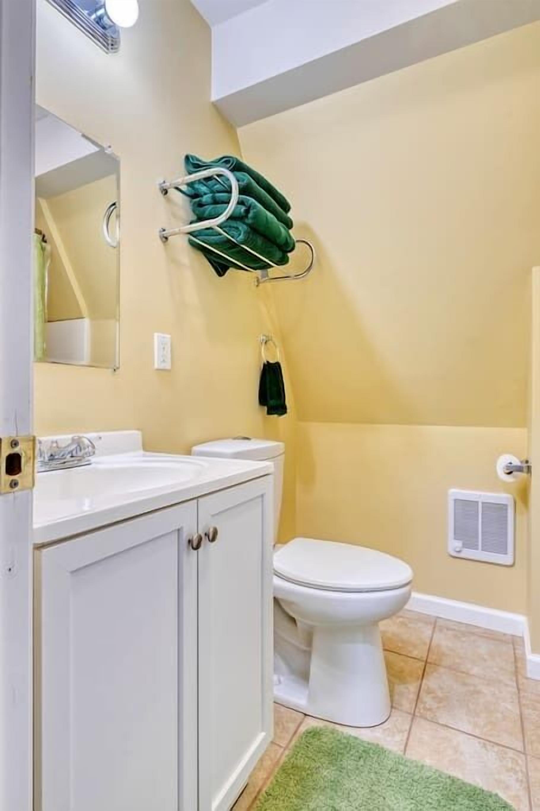 Un baño con tocador blanco, inodoro y toallero verde.