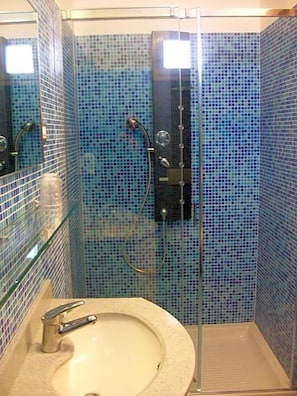 A bathroom with a glass-enclosed shower, a sink with a faucet, and tiled walls. - Hotel Mondial (Jesolo)