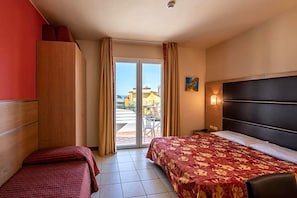 A hotel room with a bed, a wooden wardrobe, a desk, and a view through a glass door to the outside. - Hotel Mondial (Jesolo)