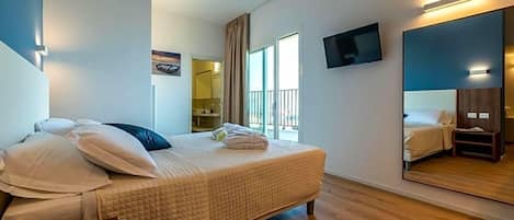 A hotel room with a bed, a flat-screen TV, a large mirror, and a window with curtains.