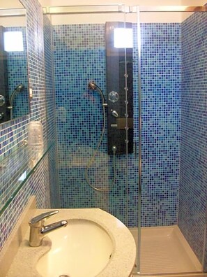 A bathroom with a glass-enclosed shower, a sink with a faucet, and tiled walls. - Hotel Mondial (Jesolo)