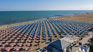 Une plage bordée de rangées de parasols bleus et rouges, une plage de sable fin et un ciel bleu azur.