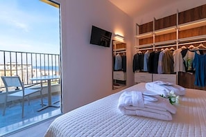 A hotel room with a balcony, a bed with white linens, a walk-in closet with hanging clothes, and a television mounted on the wall. - Hotel Mondial (Jesolo)