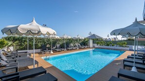 Une piscine entourée de verdure, avec des chaises longues et des parasols.