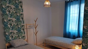 Un dormitorio con dos camas, un perchero de madera, una lámpara colgante y una ventana con cortinas azules.