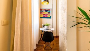 Ein schmaler Flur mit Tisch und Stühlen, einer hängenden Leuchte und einem farbenfrohen Kunstwerk an der Wand.