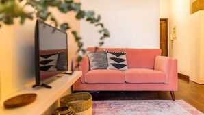 Ein gemütliches Wohnzimmer mit einem rosafarbenen Sofa, einem Flachbildfernseher und Zierkissen.
