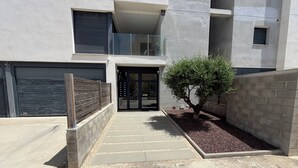 A modern building with a gated entrance, a small tree, and a concrete pathway leading to the door. - Modern apartment in superb residence with PISCINE-3 Min PLAGE ROSAS- Clim-Wifi (Roses)