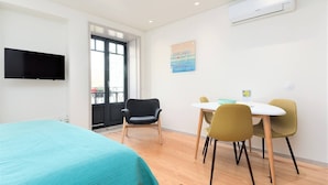 A modern hotel room with a bed, a dining table with chairs, a TV, and an air conditioning unit. - Bom Jardim - Studio with Balcony #1.2 (Porto)