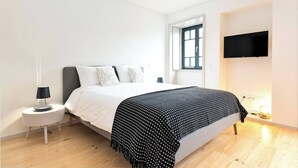 A modern bedroom with a bed, a nightstand, a TV, and a window. - Bom Jardim - Studio #2.2 (Porto)