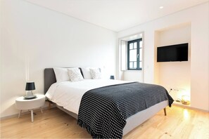 A modern bedroom with a bed, a nightstand, a TV, and a window.