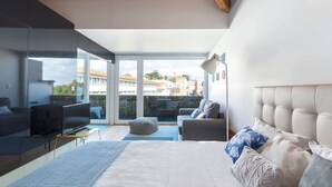 Une chambre moderne avec un grand lit, une télévision, un canapé et un balcon offrant une vue sur les immeubles.