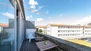 Un balcon avec un plancher en bois, une chaise en plastique blanche, une petite table sur laquelle est posée une plante en pot et un mur en pierre.