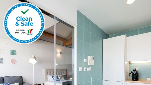 Une chambre moderne et épurée, avec un canapé gris, une table blanche sur laquelle sont disposés des articles pour le petit-déjeuner, et un coin cuisine équipé d’une machine à café.