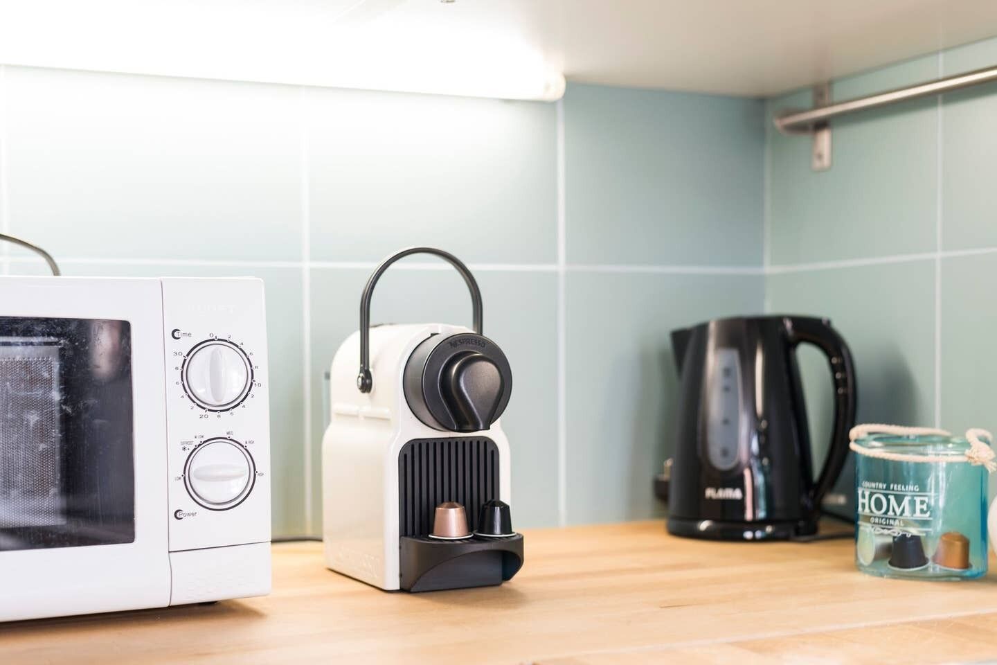 Una cocina con microondas, cafetera y hervidor sobre una encimera de madera.