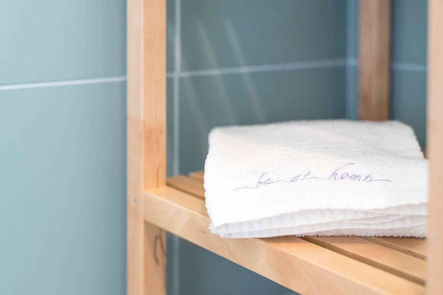 Een keurig opgevouwen witte handdoek met een handgeschreven briefje op een houten plank in een badkamer.