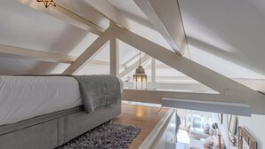 A modern loft bedroom with a sloped ceiling, a gray sofa, a patterned throw, and a wooden floor. - Oporto LightHouse Apartment by DA'HOME (Porto)