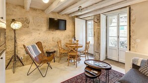 Una sala de estar acogedora con vigas de madera a la vista, una pared de piedra, un televisor de pantalla plana, un comedor con sillas de madera y un sofá.
