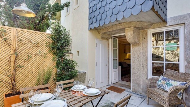 Un patio con una mesa dispuesta para cuatro, una silla de mimbre y una puerta que da a una habitación.