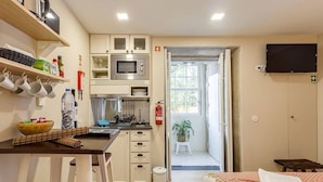 A compact kitchen with a microwave, stove, and cabinets. There is a small dining area with a table and chairs. A bed is visible in the foreground, and a TV is mounted on the wall. - Jardins da Muralha Suite Downtown by DA'HOME (Porto)