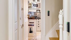 A hallway with a wooden floor leading to a kitchen area with white cabinets and a microwave. - Jardins da Muralha Suite Downtown by DA'HOME (Porto)