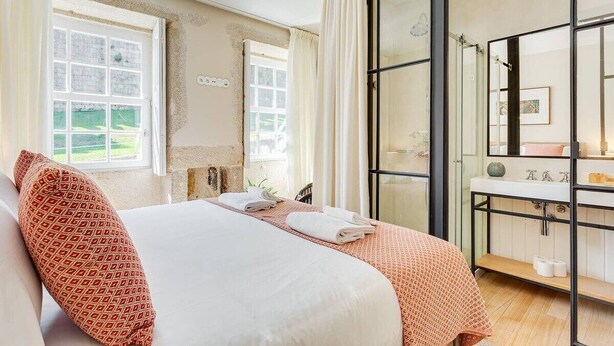 Een hotelkamer met een bed, een badkamer met een spiegel en grote ramen.