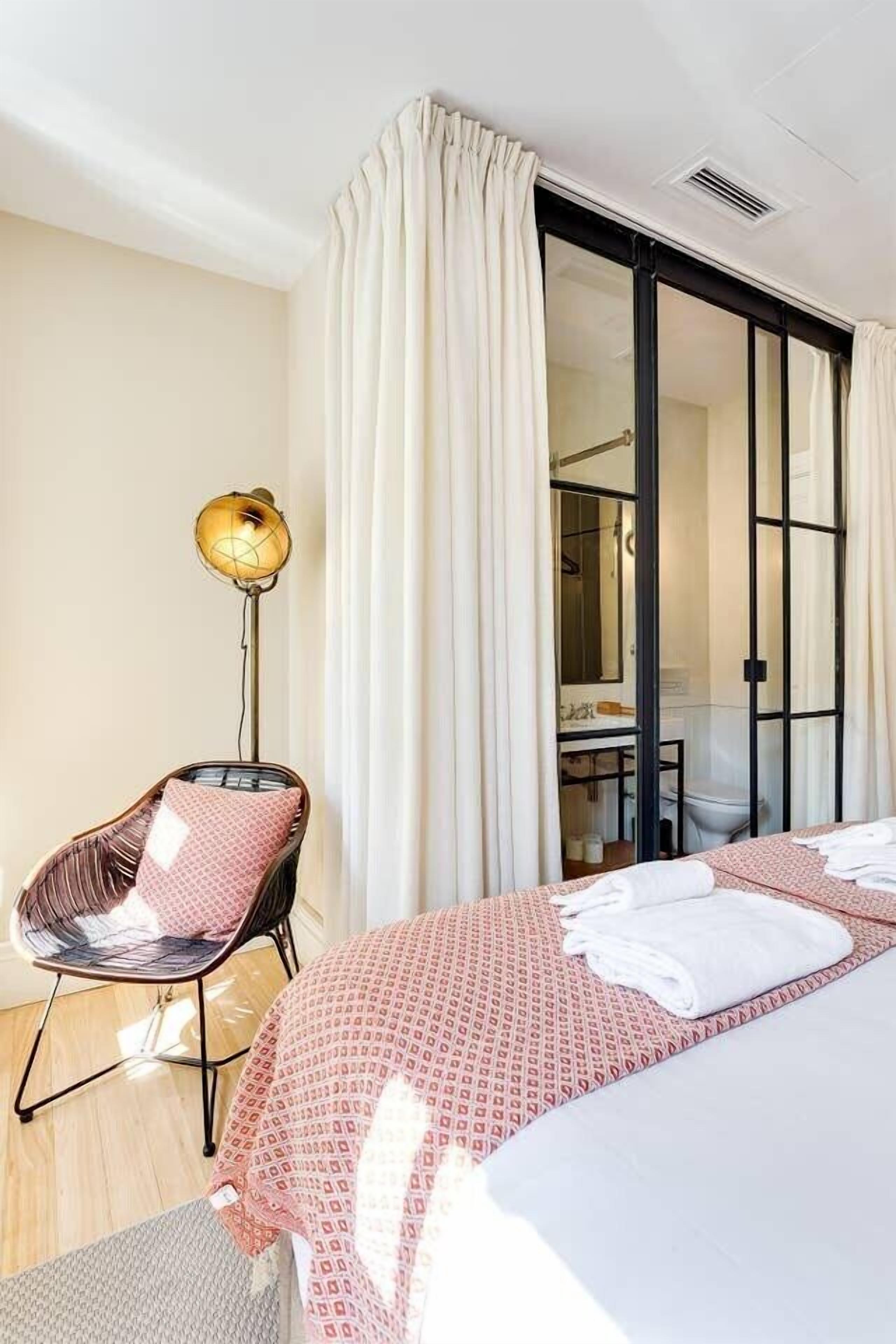 A hotel room with a bed, a chair, a floor lamp, and a sliding door leading to a bathroom.