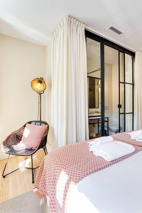 A hotel room with a bed, a chair, a floor lamp, and a sliding door leading to a bathroom.