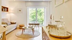 A modern living room with a sofa, a coffee table, and a dining area with a tray of glasses. - Wood Premium Downtown Apartment by DA'HOME (Porto)