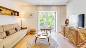 A modern living room with a sofa, a coffee table, a TV, and a balcony with a view of trees. - Wood Premium Downtown Apartment by DA'HOME (Porto)