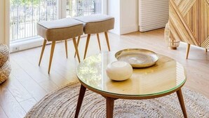 A modern living room with a glass coffee table, two cushioned chairs, a decorative wall piece, and a large window offering a view of greenery. - Wood Premium Downtown Apartment by DA'HOME (Porto)